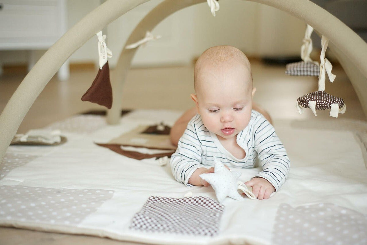 Bébé de quelques mois sur le ventre sur un tapis d'éveil