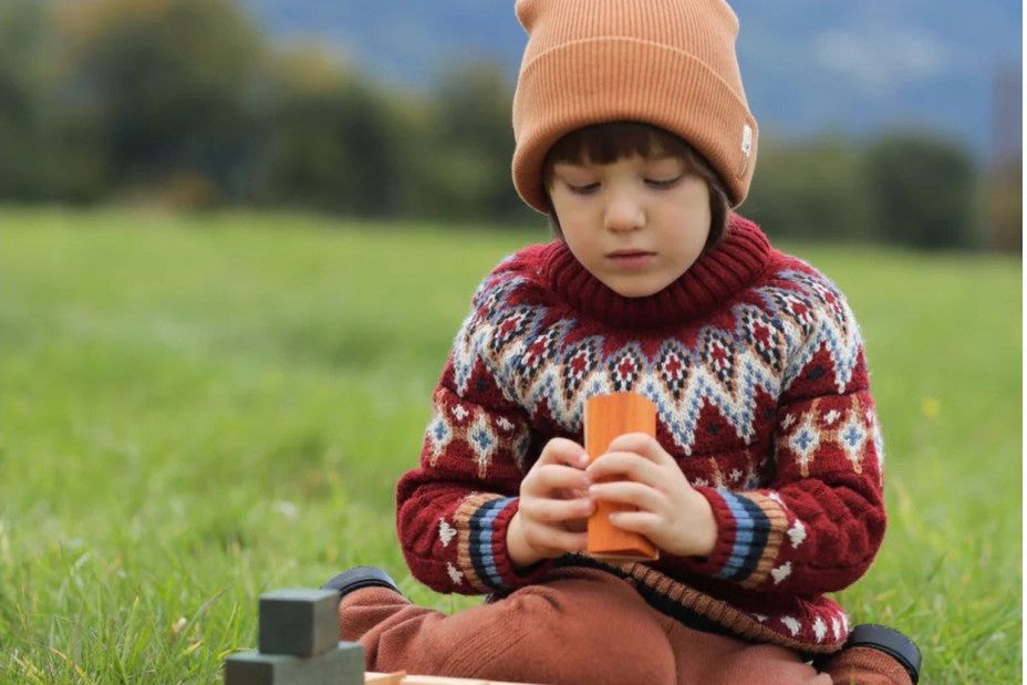 Jeune enfant en bonnet avec un chariot de marche en bois, dans l'herbe