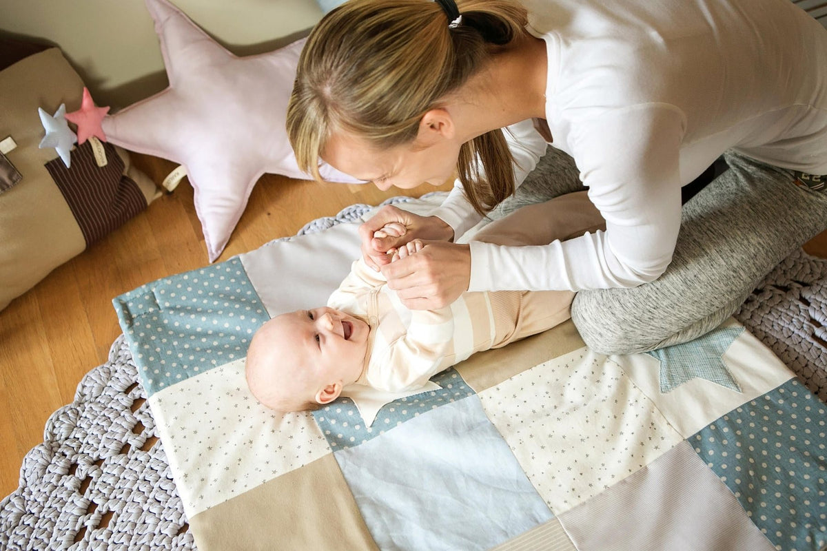 Maman penchée sur son bébé allongé sur un tapis d'éveil en patchwork bleu