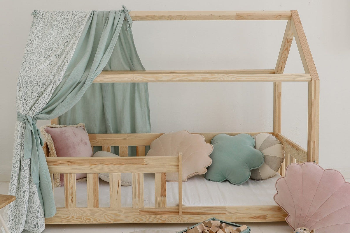 Lit cabane en bois avec voilage vert d'eau, coussins coquillages et tapis feuille clair