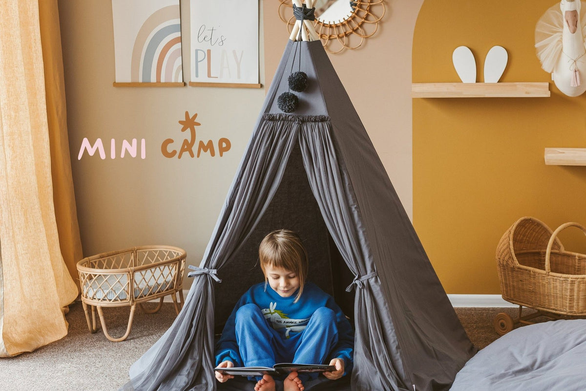 Petit garçon qui lit sous un tipi gris dans une chambre aux murs ocre