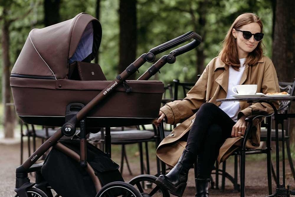 Parent assis dans un parc à côté d'une poussette avec nacelle