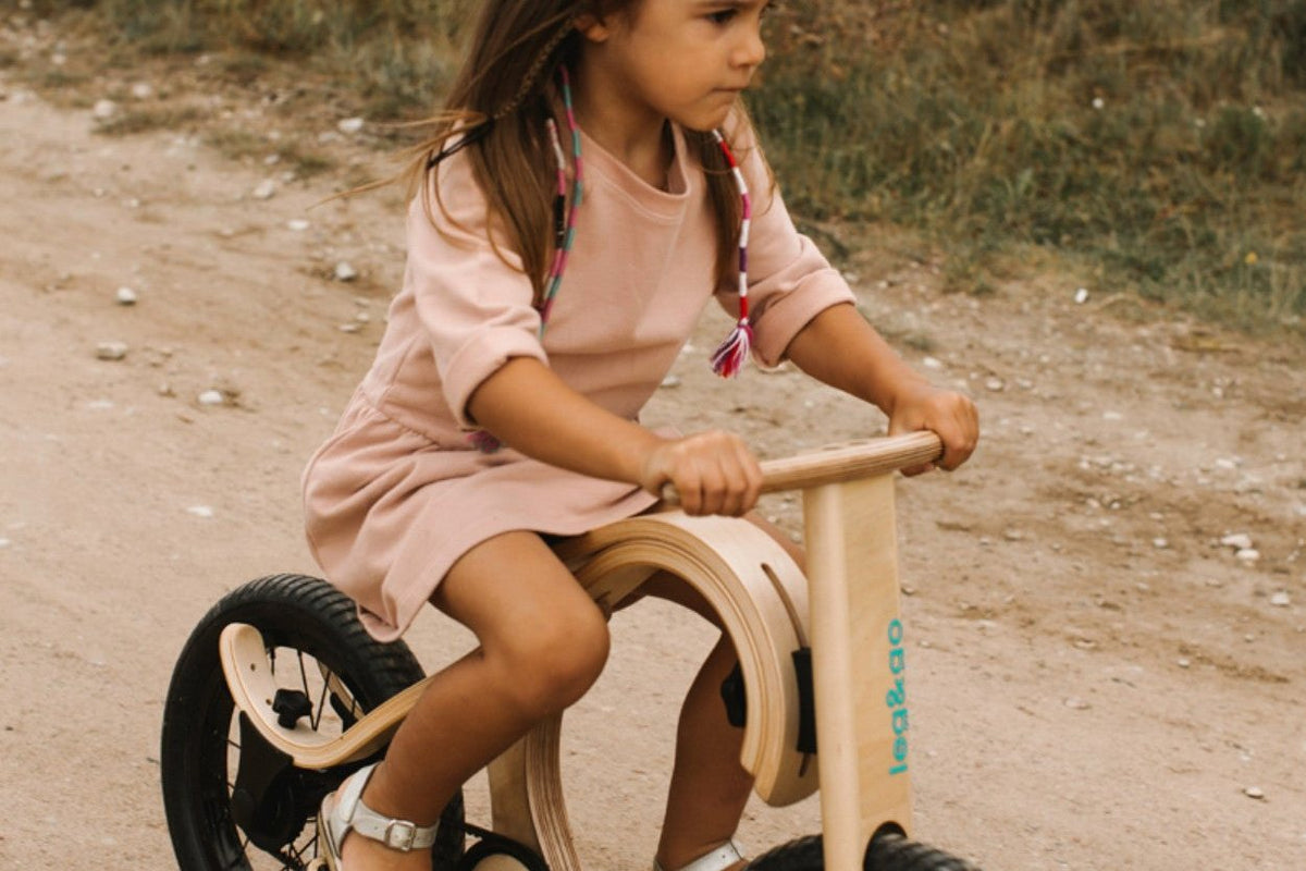 Fillette sur une draisienne en bois équipée du kit pédales, sur un chemin de terre