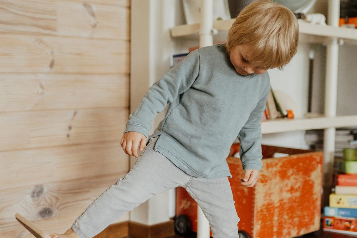 Petit garçon en équilibre sur une planche courbe en bois, dans le salon