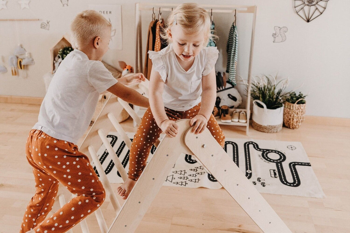 Deux enfants qui escaladent un triangle de Pikler en bois dans une chambre lumineuse
