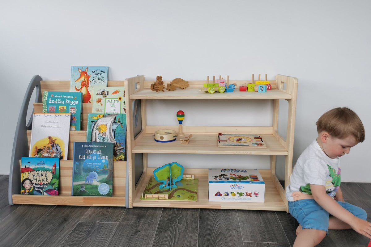 Petit garçon assis devant une étagère basse en pin avec livres de face et jouets