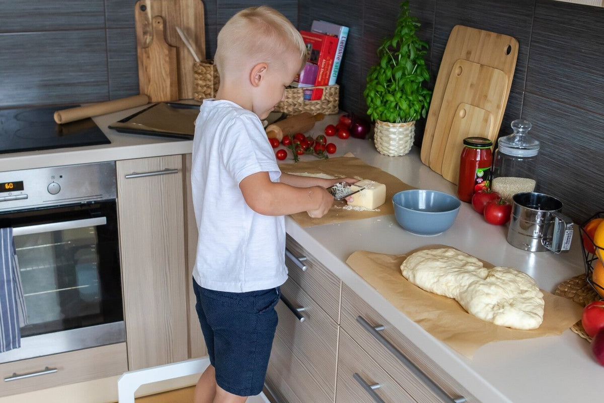 Petit garçon debout sur une chaise Montessori pour pétrir la pâte au plan de travail