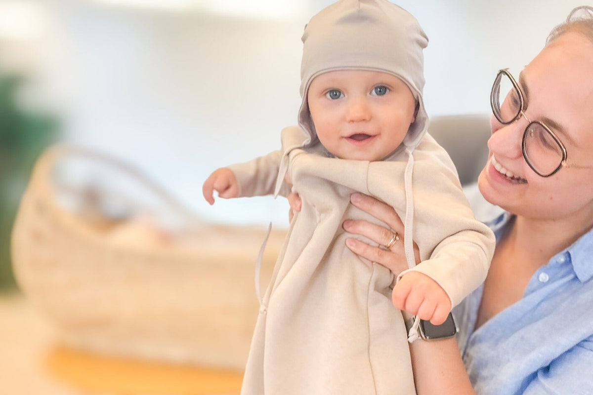 Maman qui tient son bébé en gigoteuse à manches beige et bonnet assorti