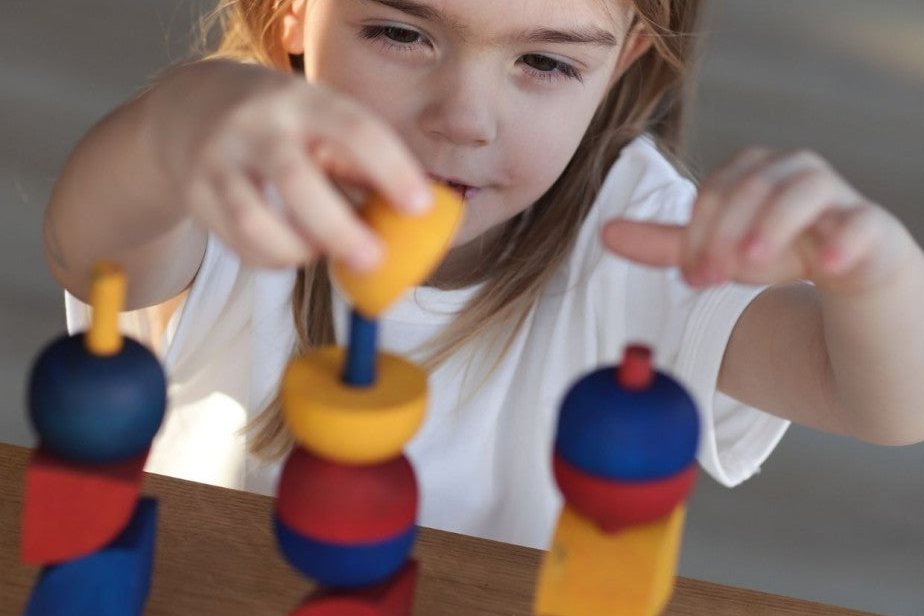 Fillette concentrée qui empile des pièces en bois colorées sur un jeu à tiges