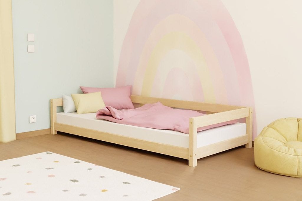 Lit Montessori bas en bois devant un mur peint d'un arc-en-ciel
