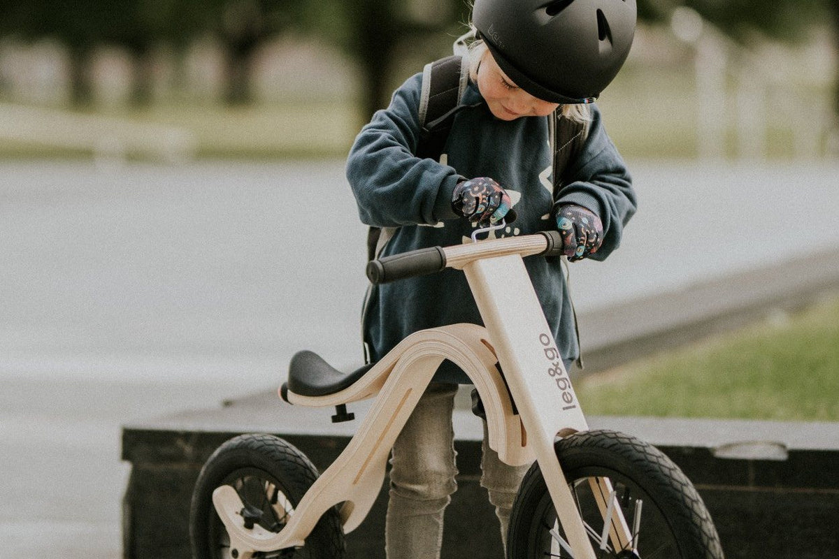Enfant casqué sur une draisienne évolutive en bois, au bord d'une rue