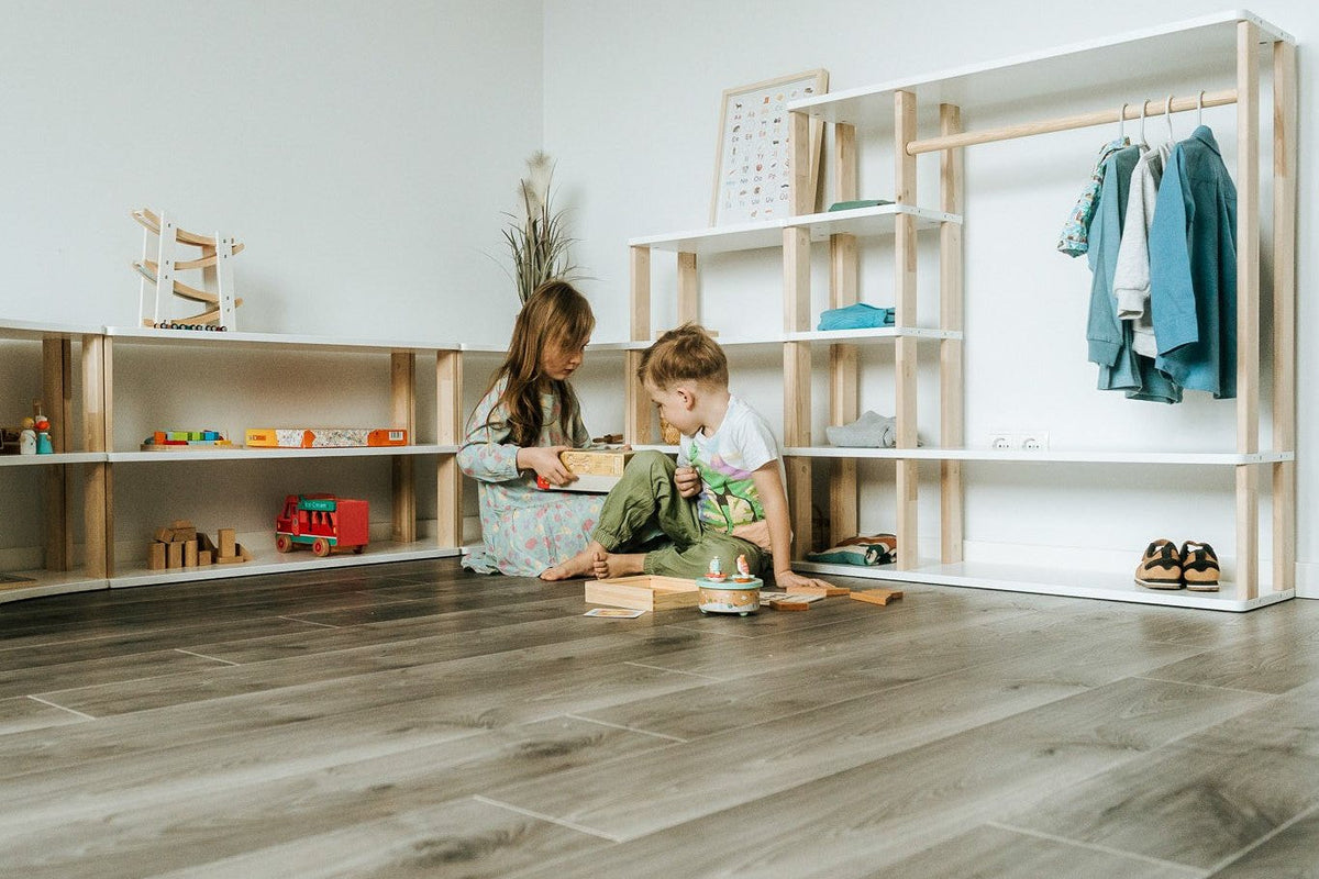 Deux enfants qui jouent par terre devant des étagères basses Montessori en pin
