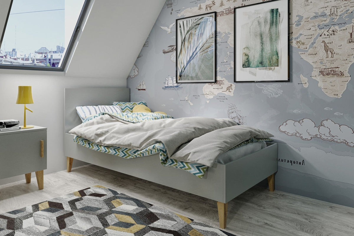 Lit enfant gris avec couette froissée dans une chambre mansardée aux murs décorés d'une carte