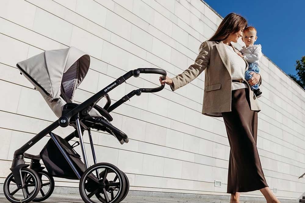 Maman avec son bébé dans les bras qui pousse une poussette le long d'un mur