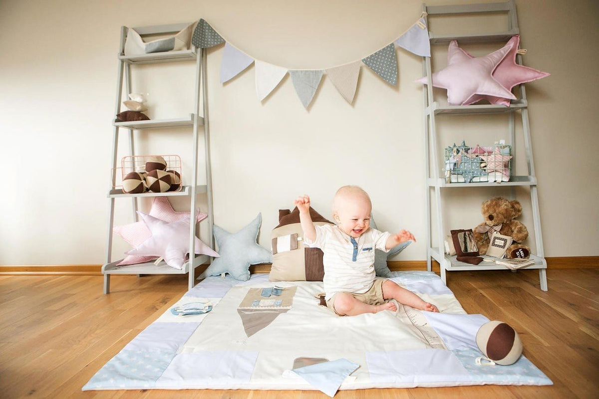 Bébé assis sur un tapis d'éveil en coton bio, entre deux étagères décorées de fanions