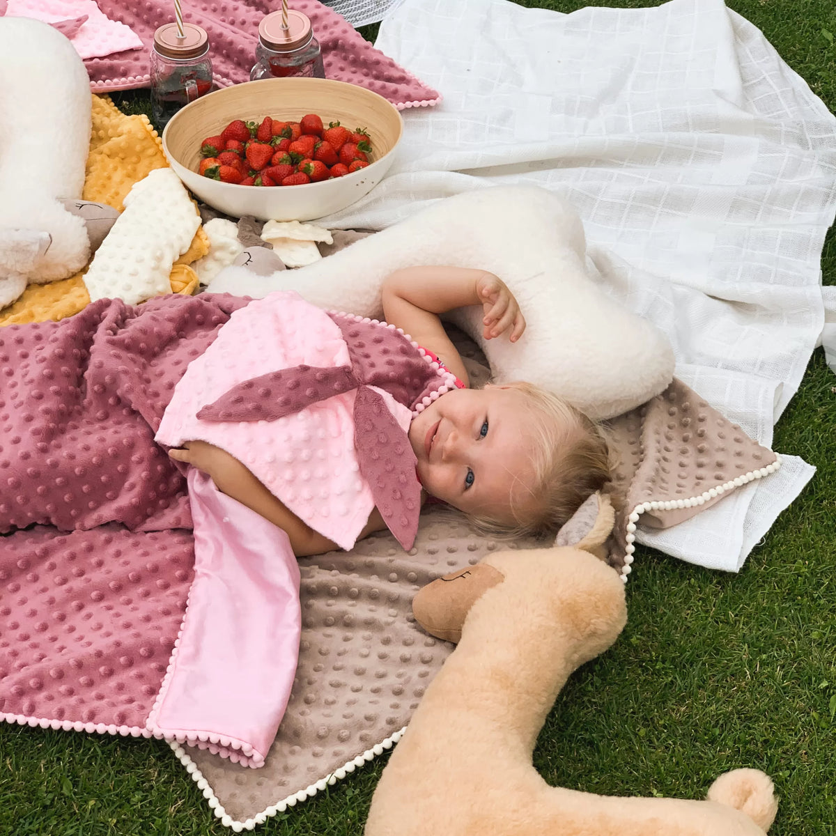 Une petite fille allongée dans l'herbe parmi des peluches coussins Kai aš mažas buvau
