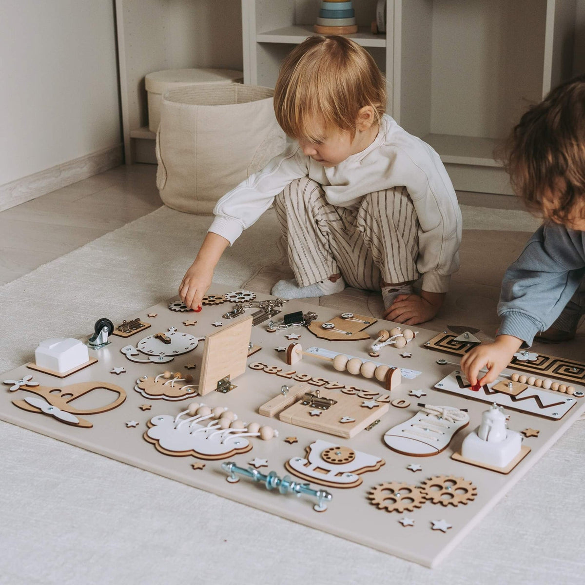Deux enfants manipulent un busy board BusyBunnyToys posé au sol
