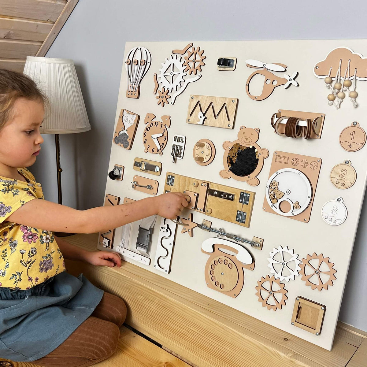 Une petite fille ouvre un loquet sur un grand busy board BusyBunnyToys