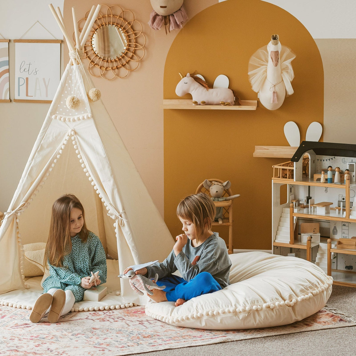 Deux enfants lisent devant un tipi Minicamp à pompons, sur un grand coussin de sol