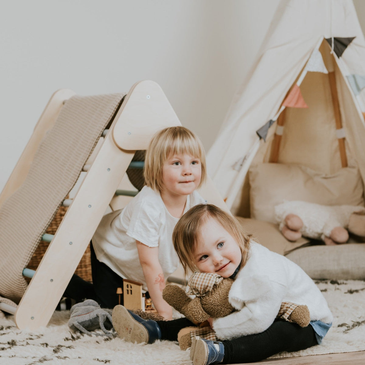 Dos niños jugando junto a un triángulo de escalada y un tipi