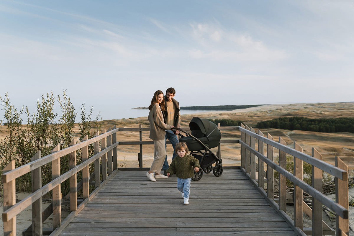 Des parents et leur enfant sur une passerelle en bord de mer avec une poussette Noordi
