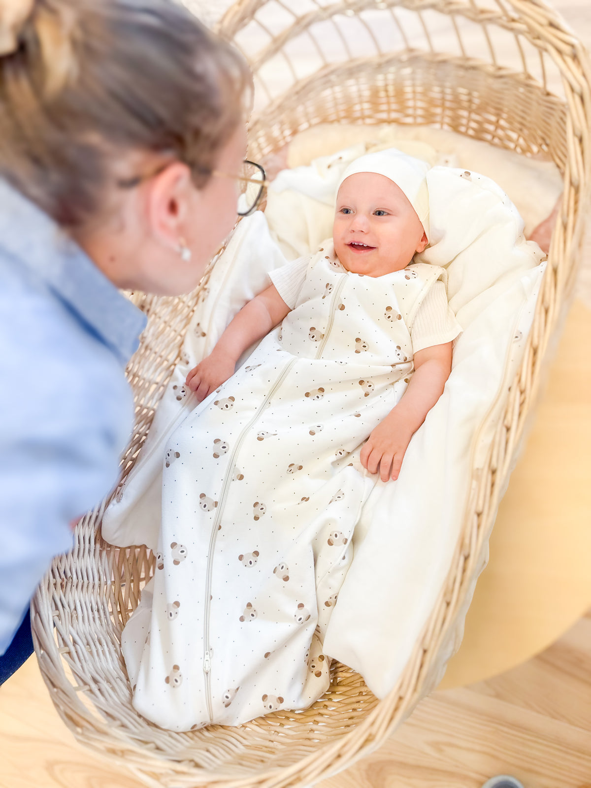 Un bébé en gigoteuse Lenne dans un couffin, sous le regard de sa maman